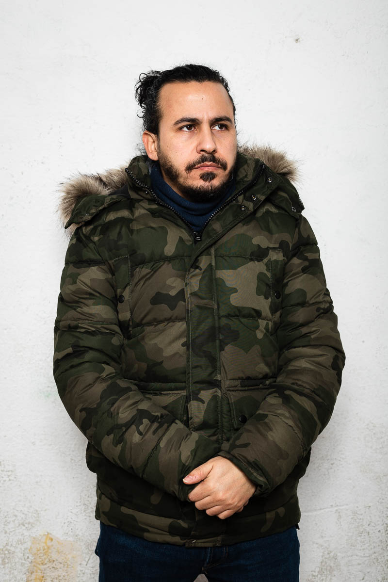 Portrait of refugee Wasim with his hands clasped wearing a camo puffer jacket
