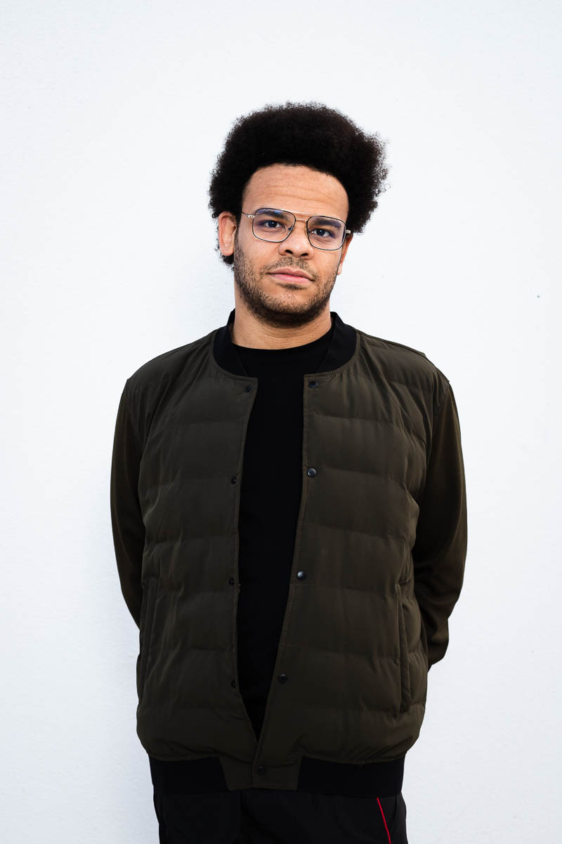 Portrait of refugee Elsayed standing with his hands behind his back and wearing a black puffer jacket
