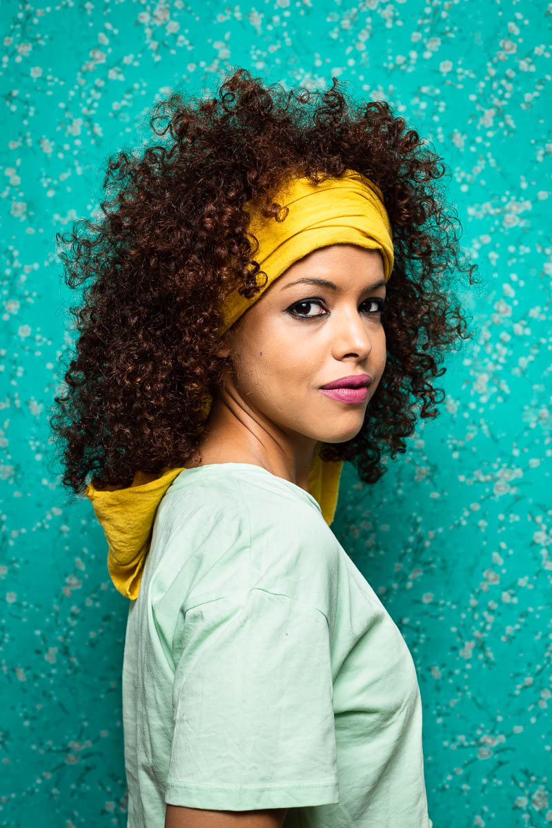 Portrait of refugee Ebbaba turned sideways with her face turned to the camera with her curly hair tied with a bandana scarf
