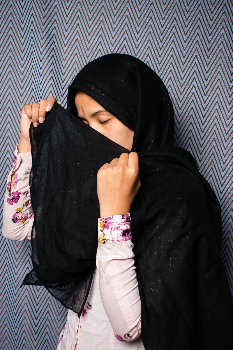Portrait of refugee Asiyh with her eyes closed and using her black hijab to hide the lower half of her face