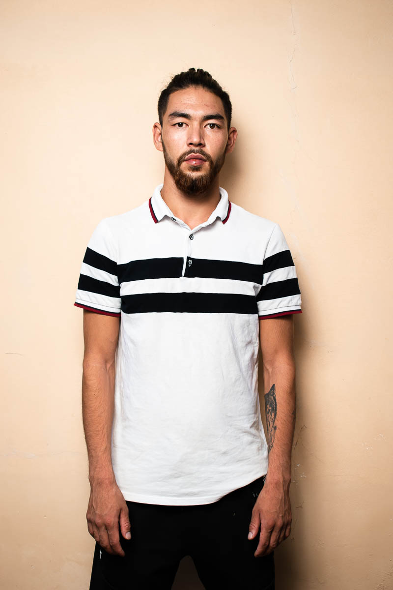 Portrait of refugee Ali wearing a white polo shirt with black stripes