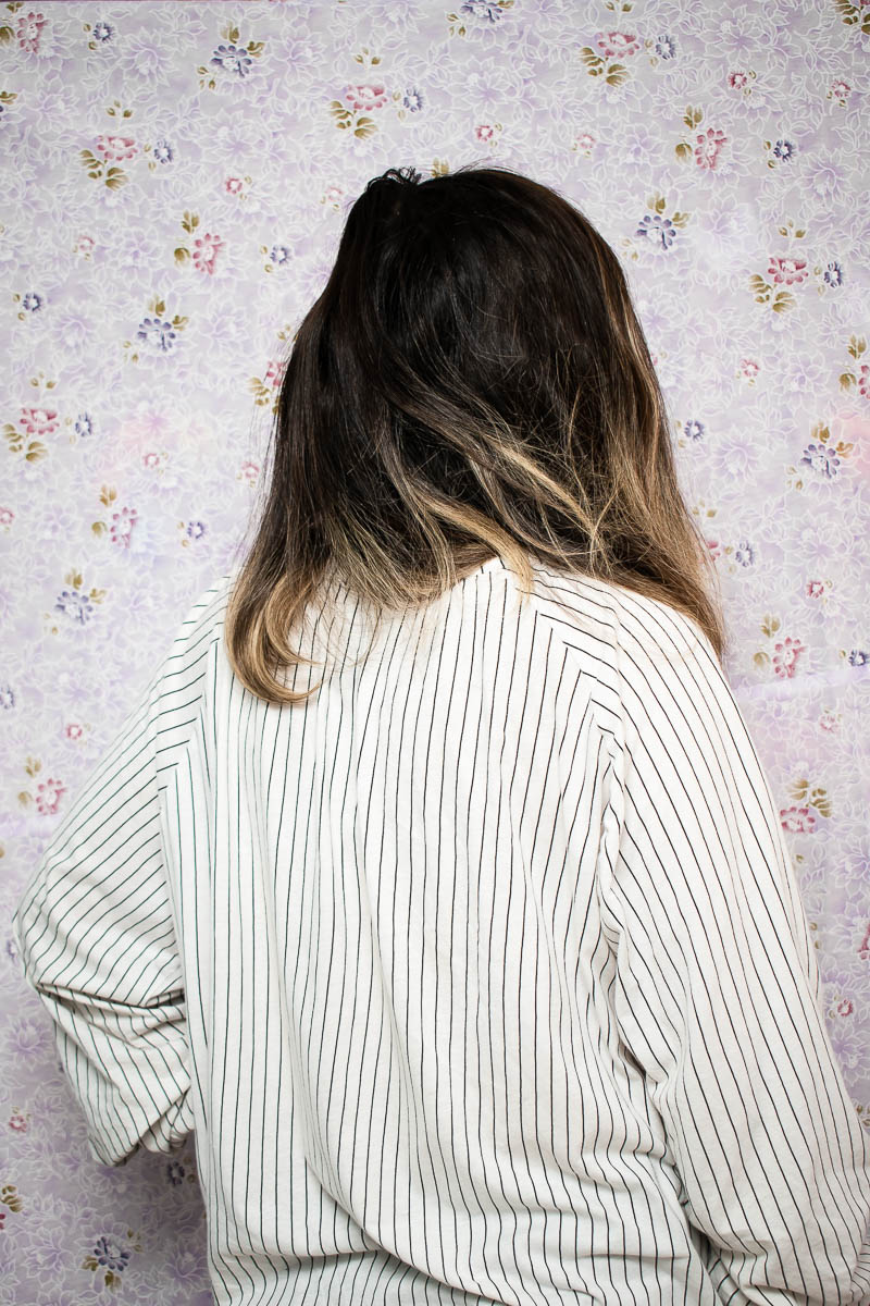Portrait of refugee Ameneh wearing a striped shirt with her back to the camera