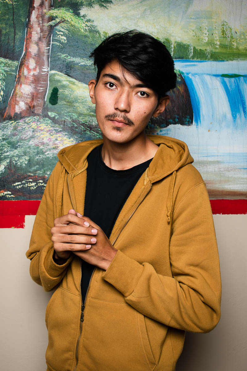 Portrait of refugee Yaser wearing a brown hoodie jacket with his hands clasped