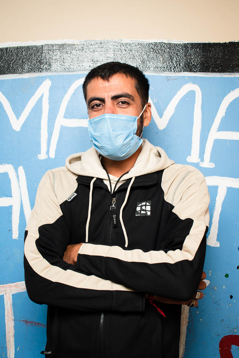 Portrait of refugee Fez wearing a face mask and standing with his hands crossed