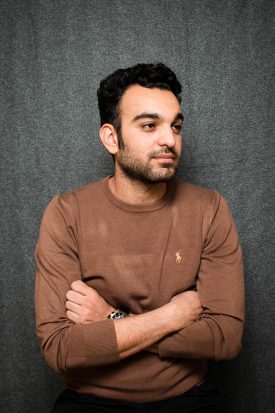 Portrait of refugee Ewdvard looking to his left with his hands crossed