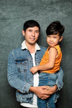 Portrait of refugee Morteza smiling while holding a child in his arms