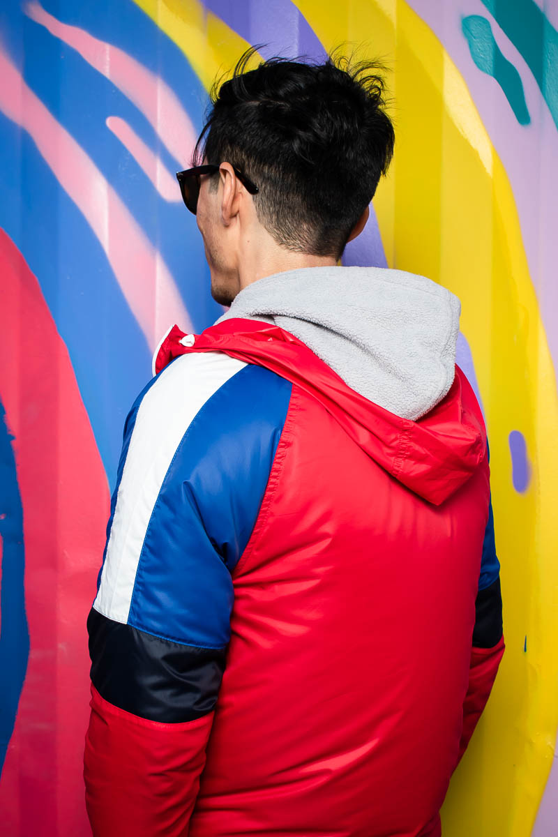Portrait of refugee Mohammad wearing a colourful hoodie with his back towards the camera standing against a graffiti wall