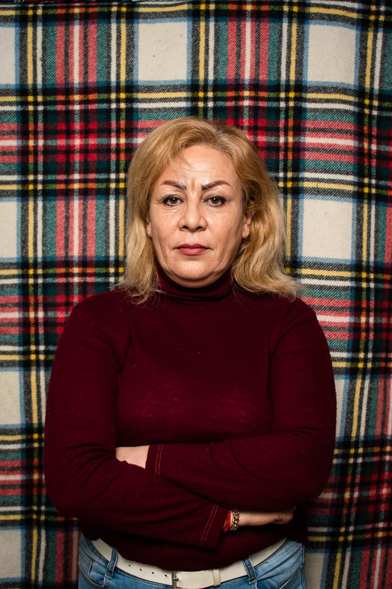 Portrait of refugee Golzar wearing a maroon turtleneck with her arms crossed standing against a plaid background
