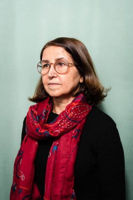 Portrait of refugee Katayon with a red scarf wrapped around her neck standing facing her right