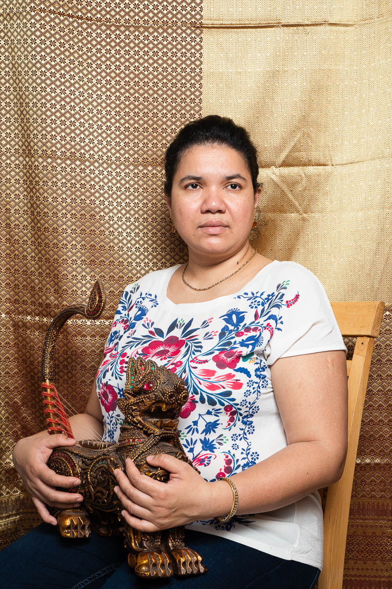 Portrait of refugee Khin sitting and holding a Burmese Chinthe figurine