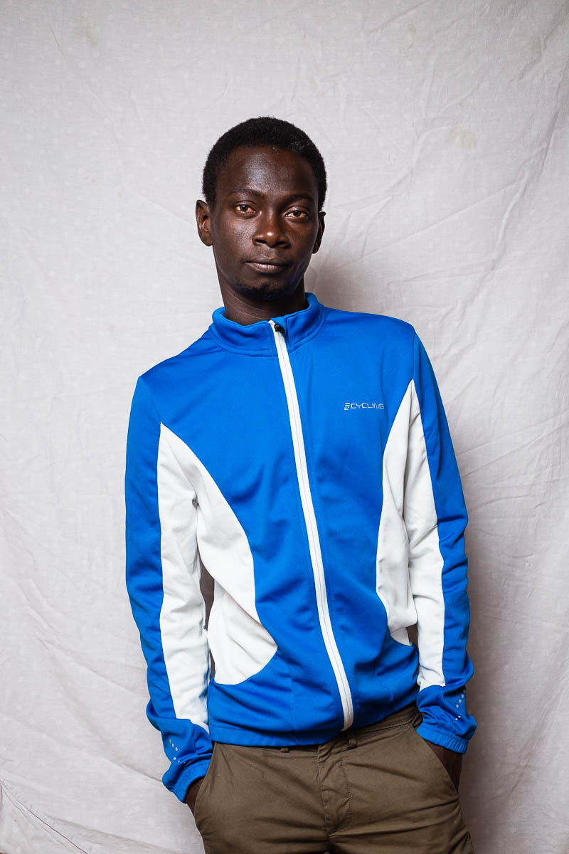 Portrait of refugee Lamin wearing a blue jacket with his hands in the pockets of his pants