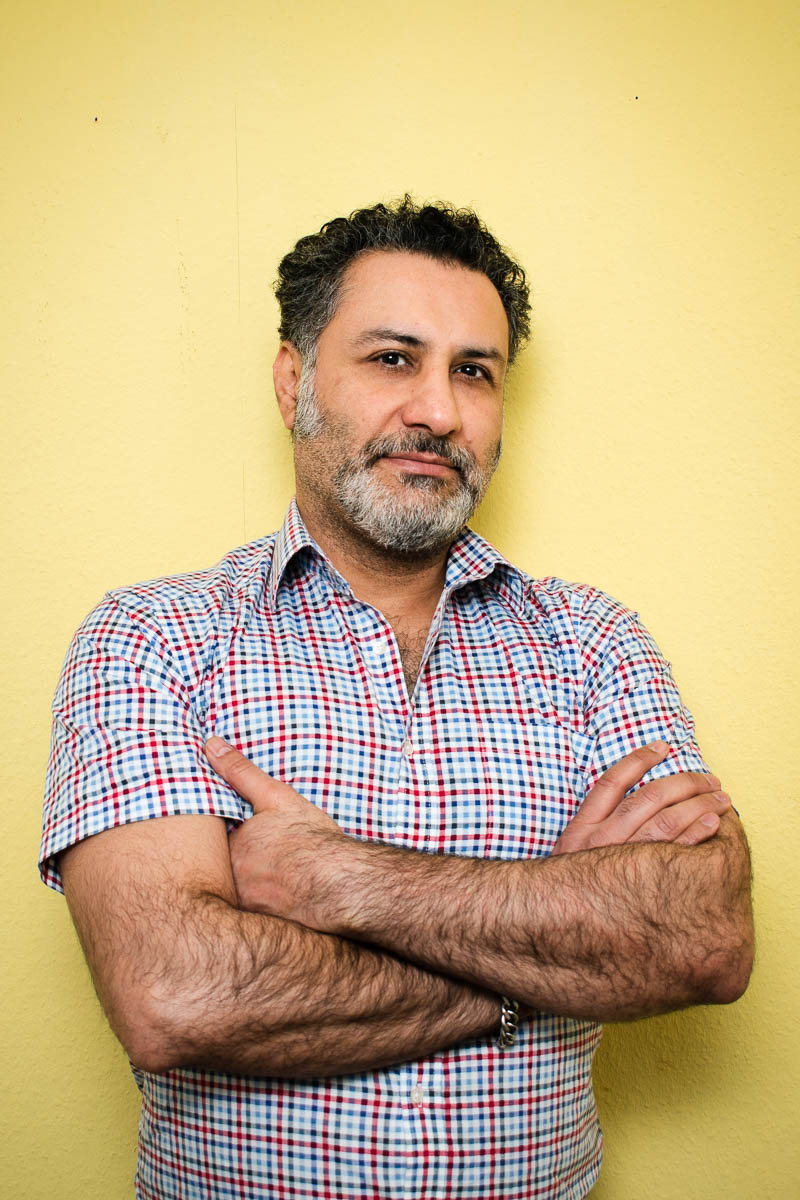 Portrait of refugee Nikjoo wearing a plaid shirt with his arms crossed across his chest