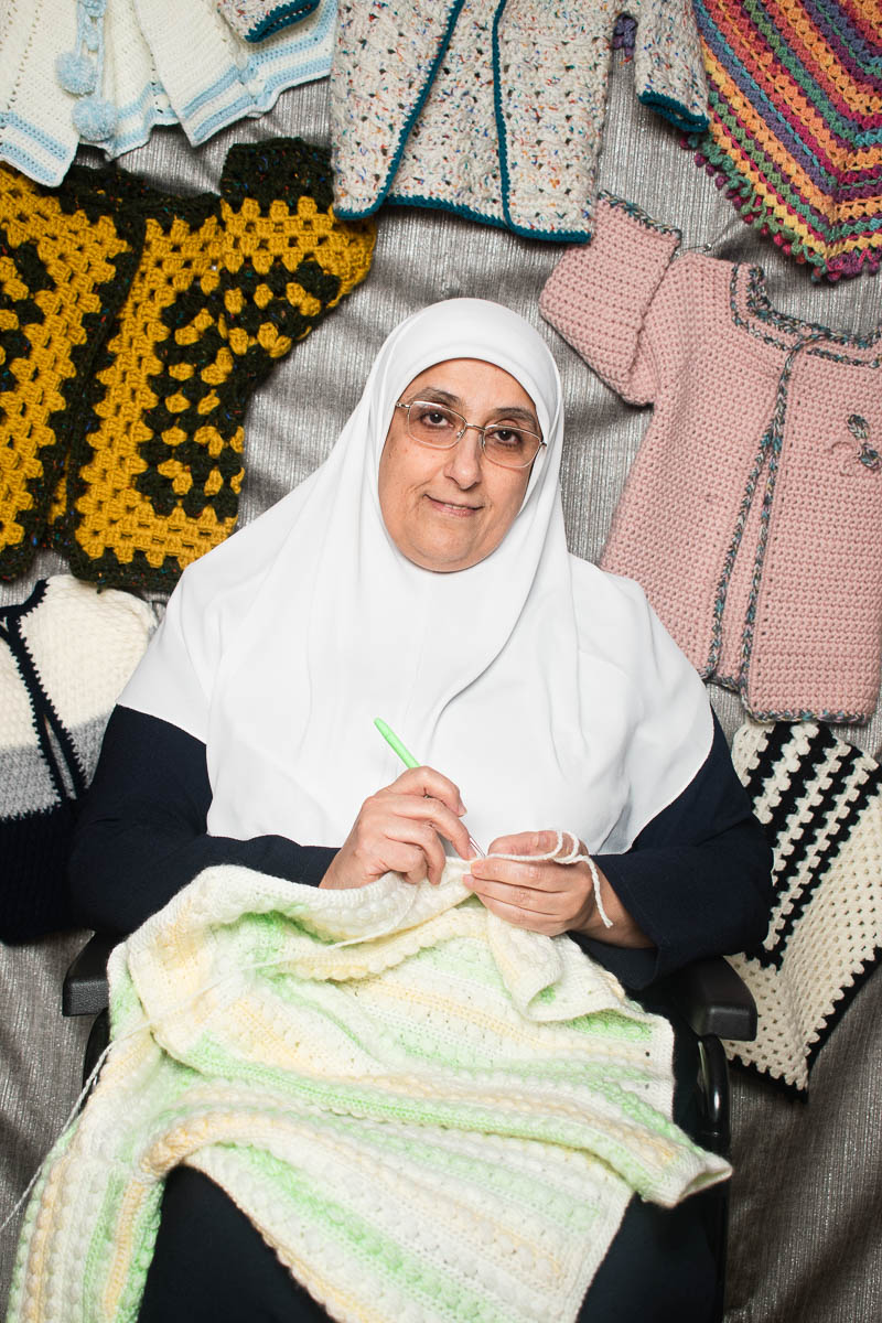 Portrait of refugee Nadia sitting on a chair and knitting