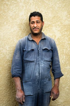 Portrait of refugee Lassaad with his hands and blue overall covered in white dust