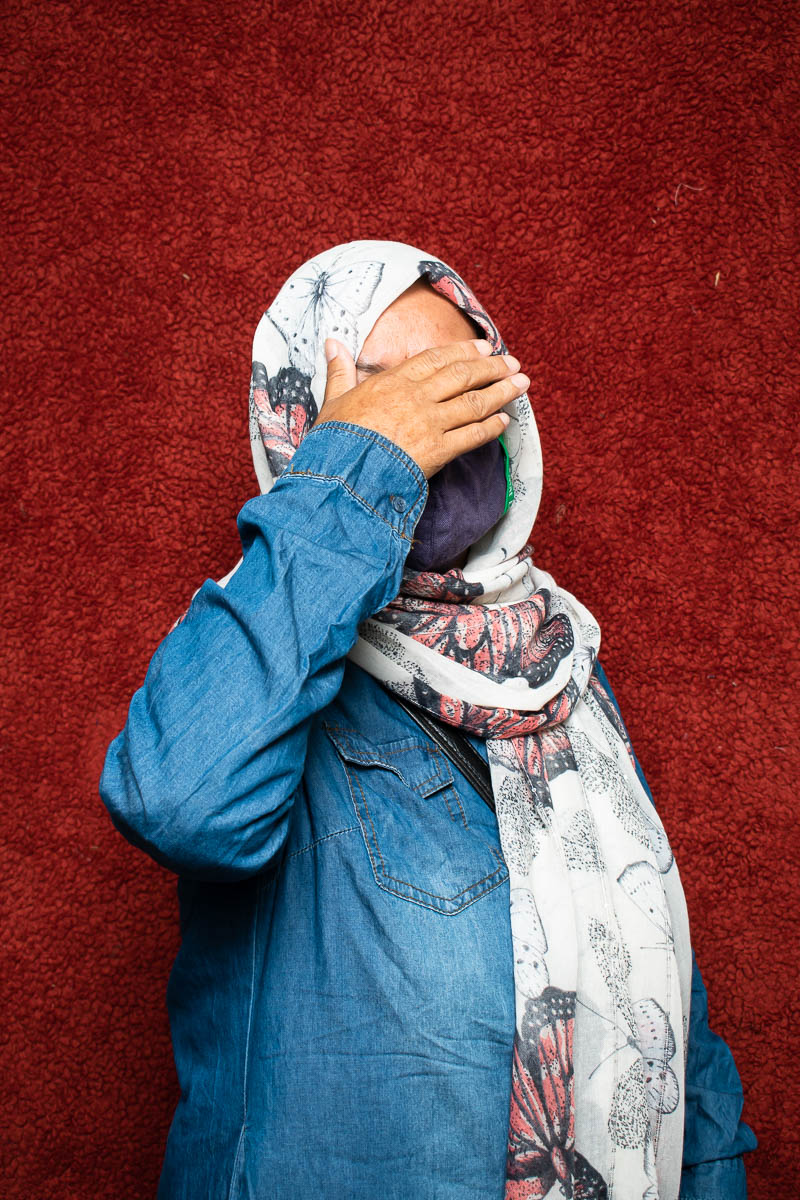 Portrait of refugee Kobra wearing a hijab and face mask using her right hand to hide her eyes