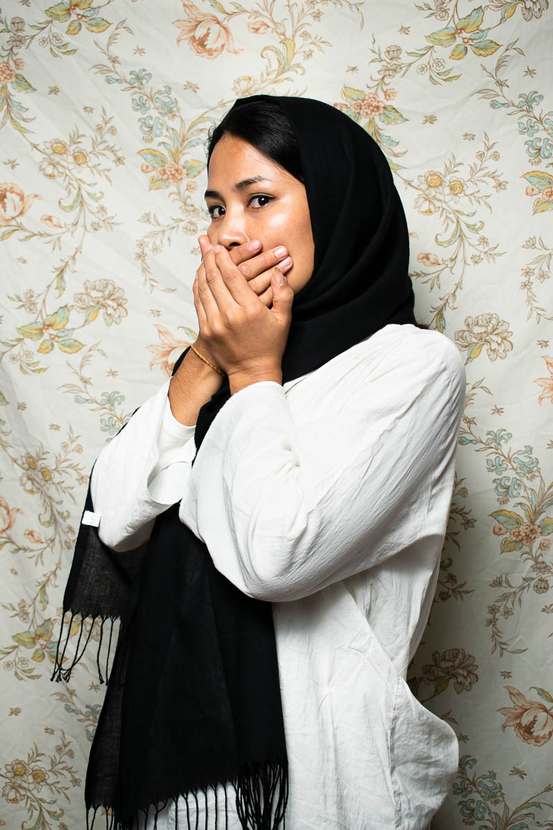 Portrait of refugee Masome wearing a black hijab and both her hands covering her mouth