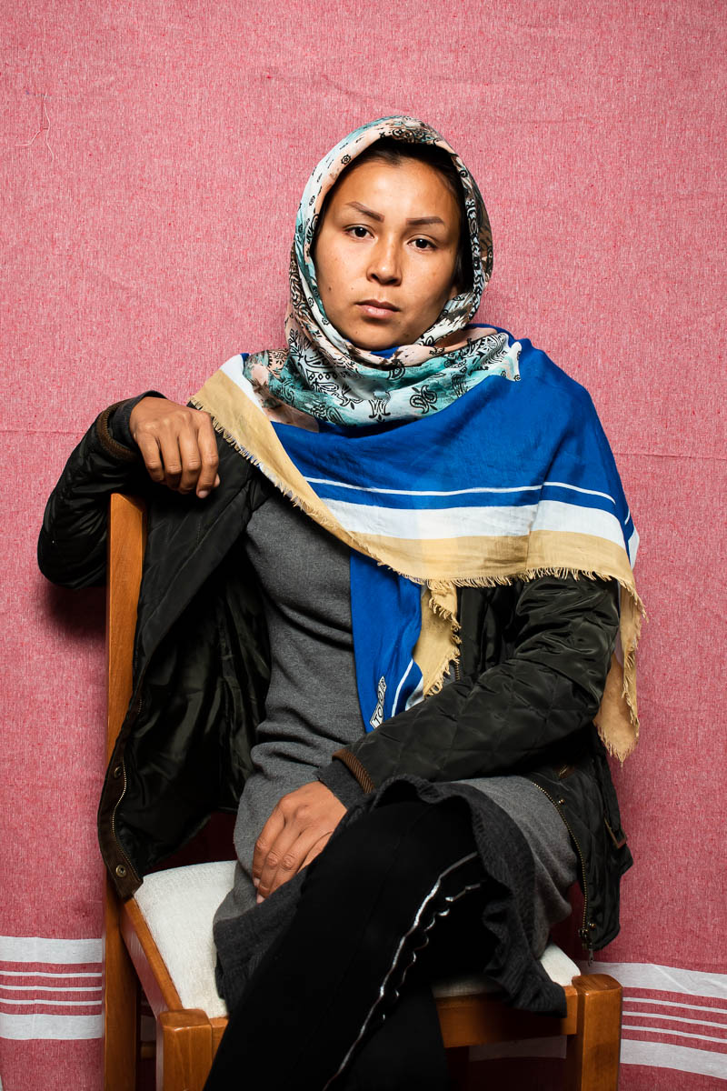 Portrait of refugee Atefe sitting on a chair with one hand on the chair and the other on top of her crossed legs