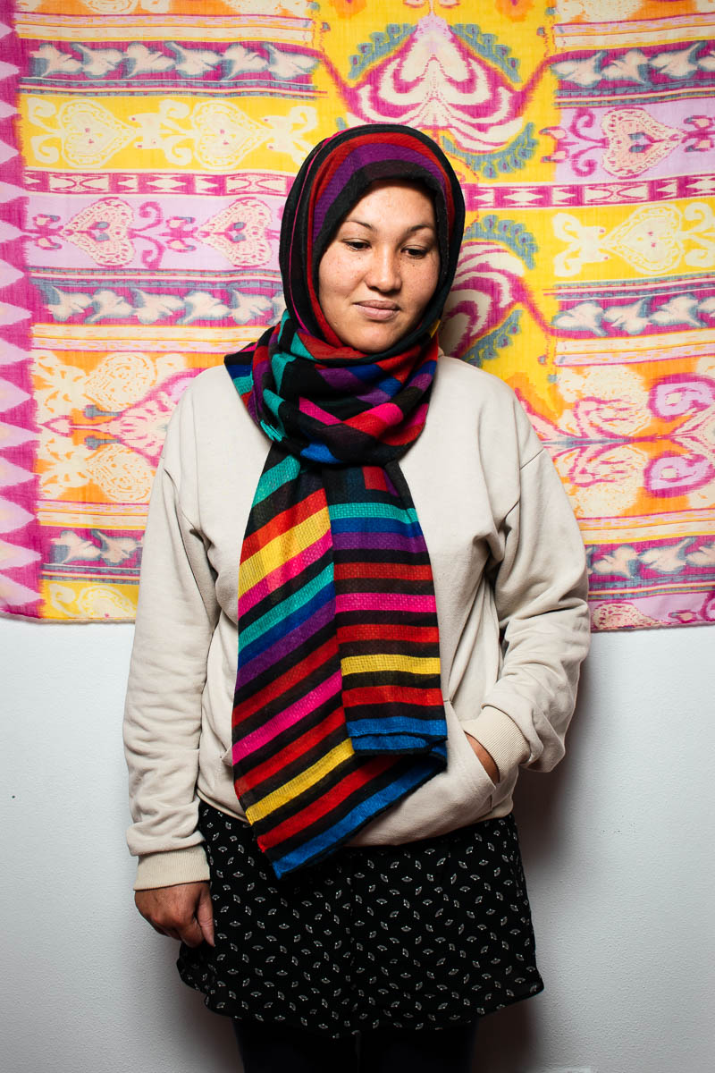 Portrait of refugee Mohadese wearing a colorful hijab with her hand in her hoodie pocket looking down and smiling