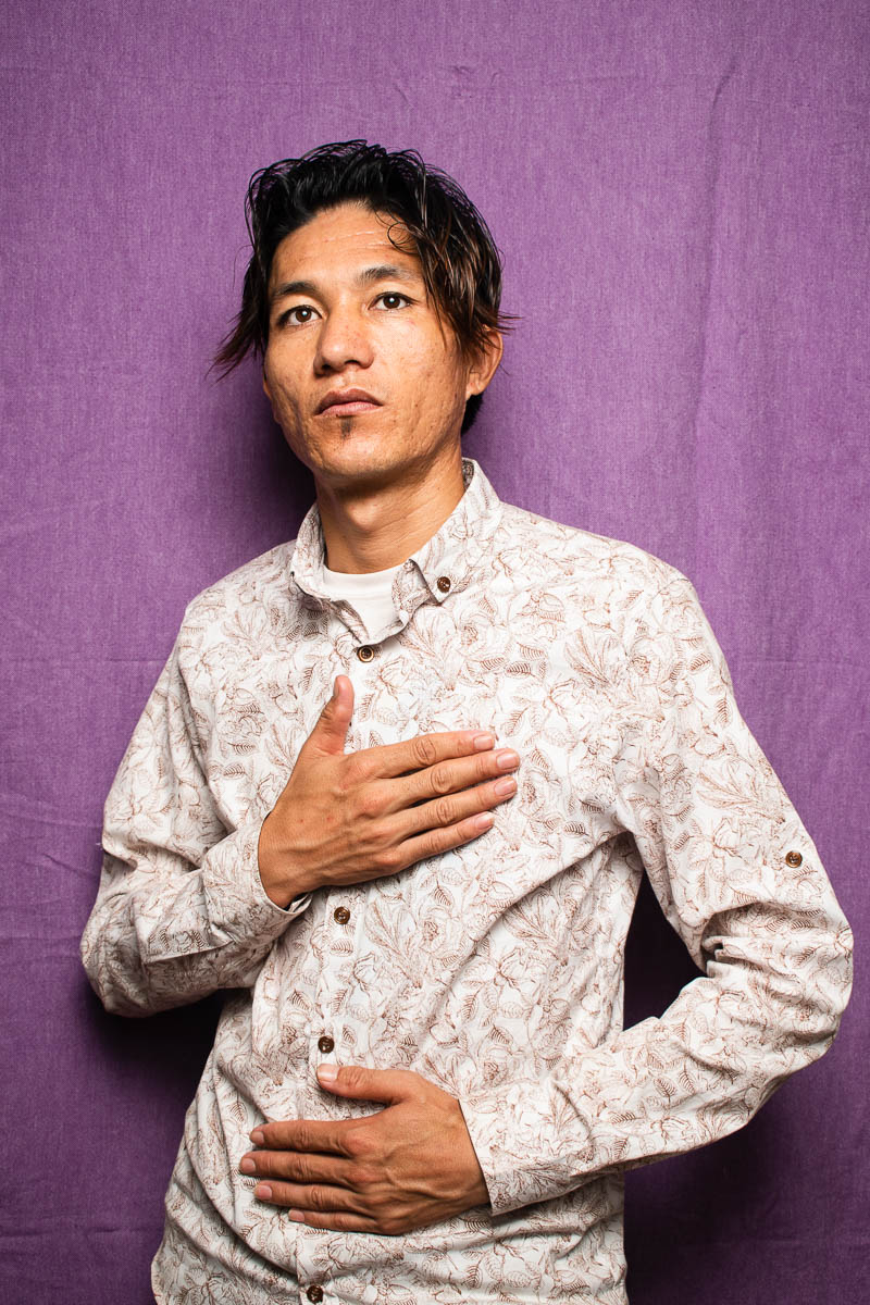 Portrait of refugee Najib with one hand on his chest and one hand on his stomach