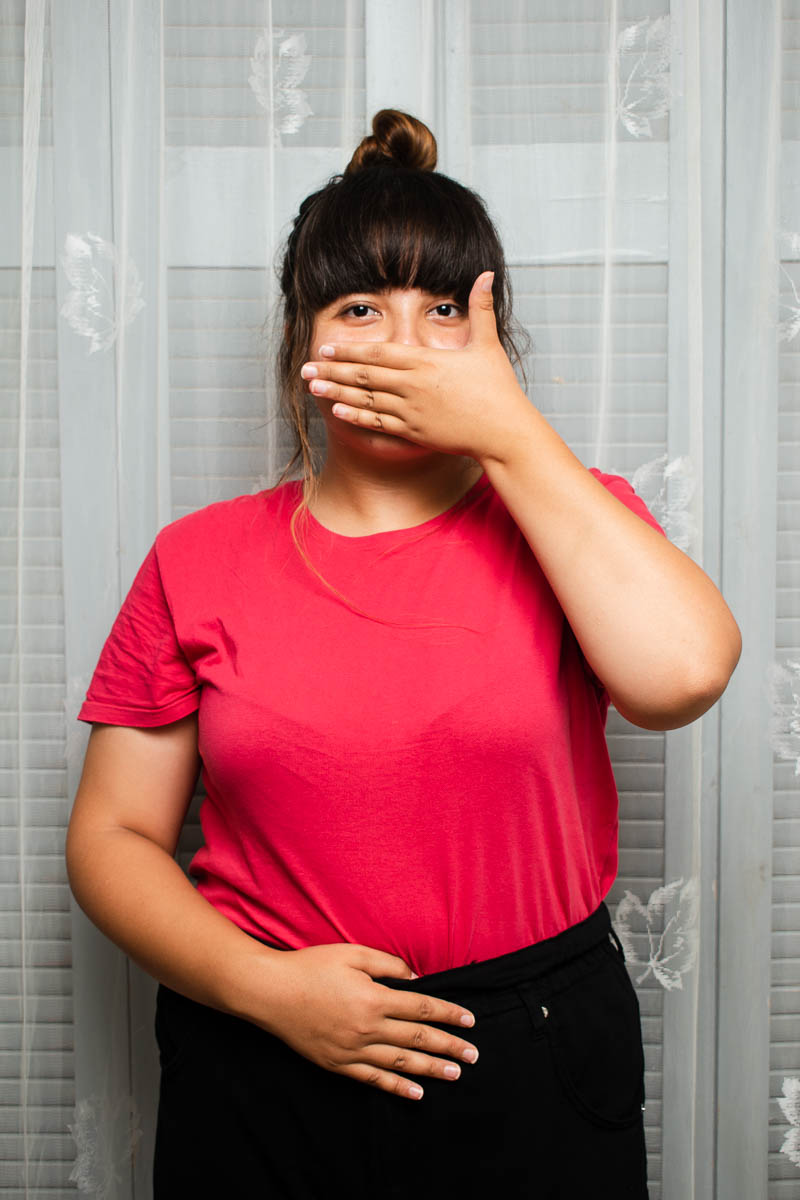 Portrait of refugee Atefeh with one hand covering the lower half of her face and the other hand on her stomach