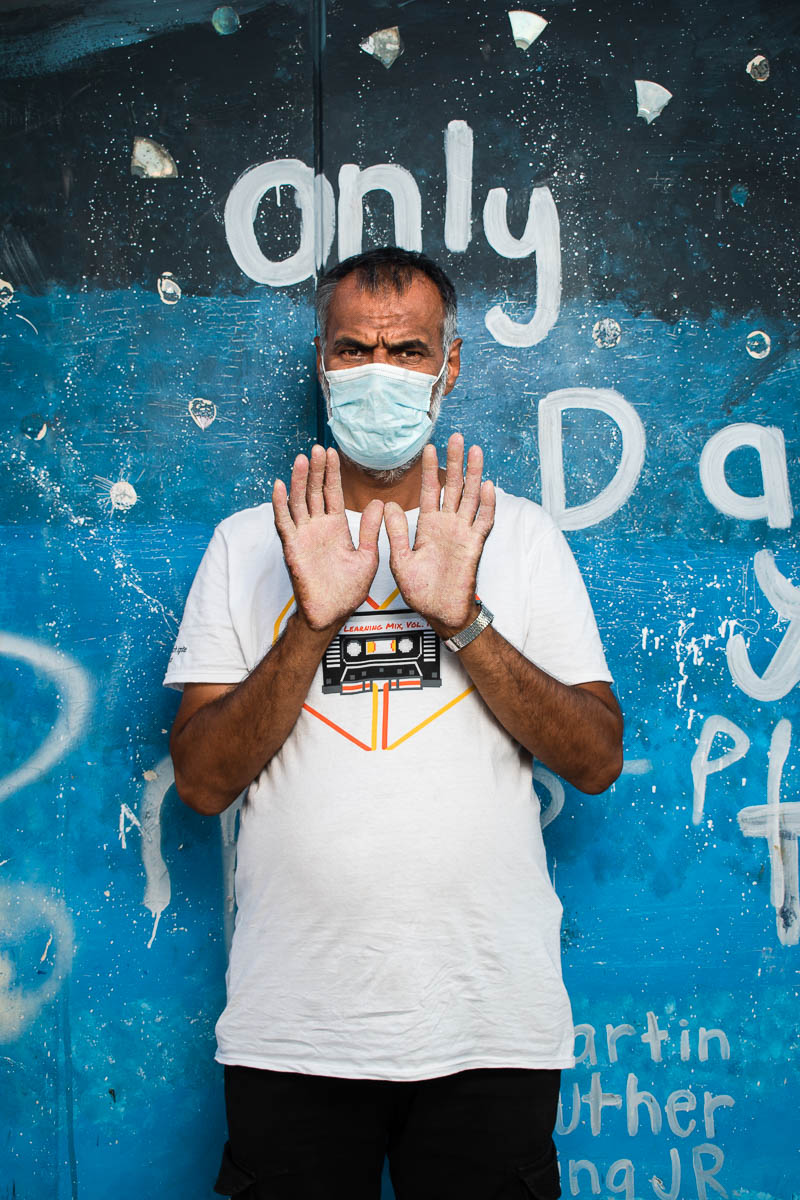 Portrait of refugee Mohamad wearing a face mask his hands together showing both his palms to the camera