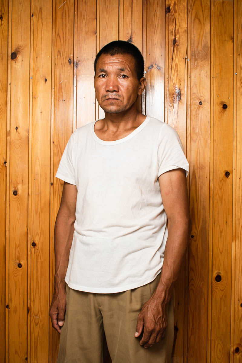 Portrait of refugee Mohamad standing against a wooden planked wall