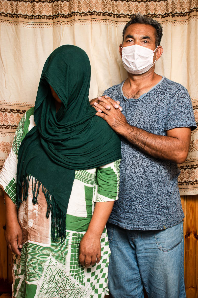 Portrait of refugee Naser standing with his interlocked hands resting on the shoulder of a woman whose face is completely covered with a green draped scarf