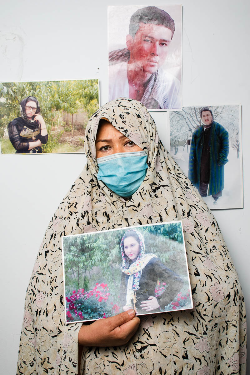 Portrait of refugee Sakineh wearing a long hijab and face mask holding a realistic hand drawn portrait of a lady in a garden