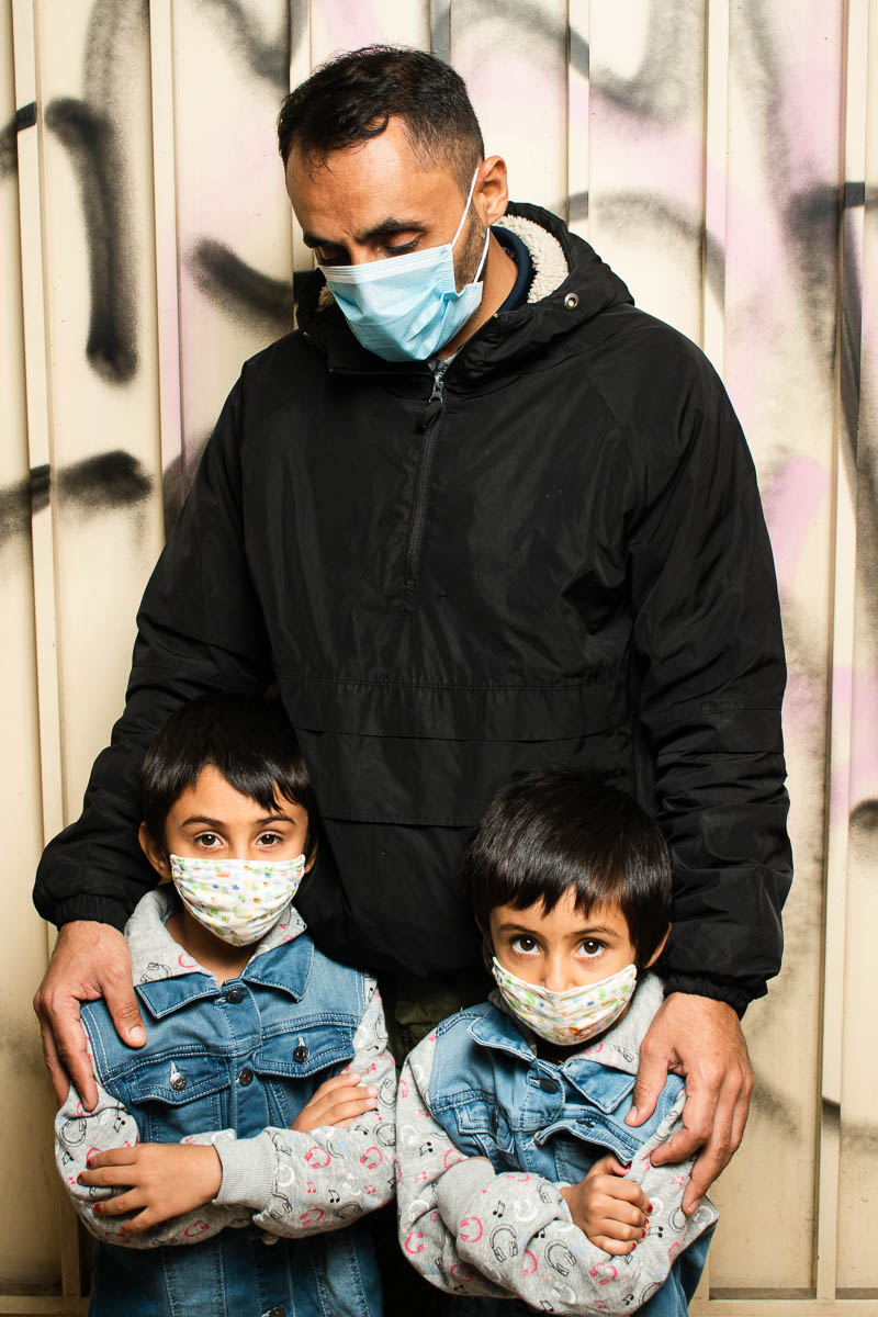 Portrait of refugee Mirwais holding two kids and looking down at them