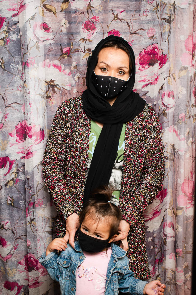 Portrait of refugee Najibeh wearing a black hijab and face mask holding a small child