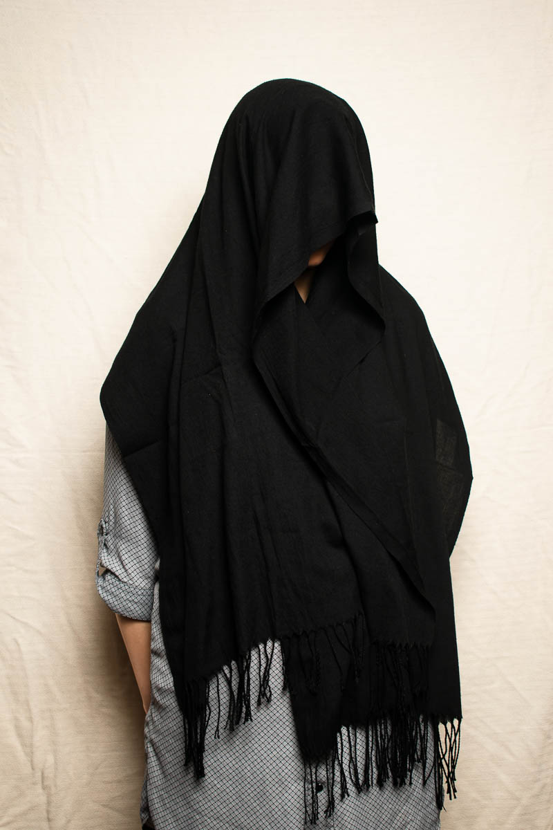 Portrait of refugee Sahar with a draped black scarf covering her face and body