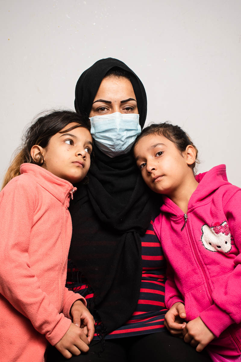 Portrait of refugee Shokriye wearing a hijab and face mask with two kids wearing pink jackets standing on both her sides
