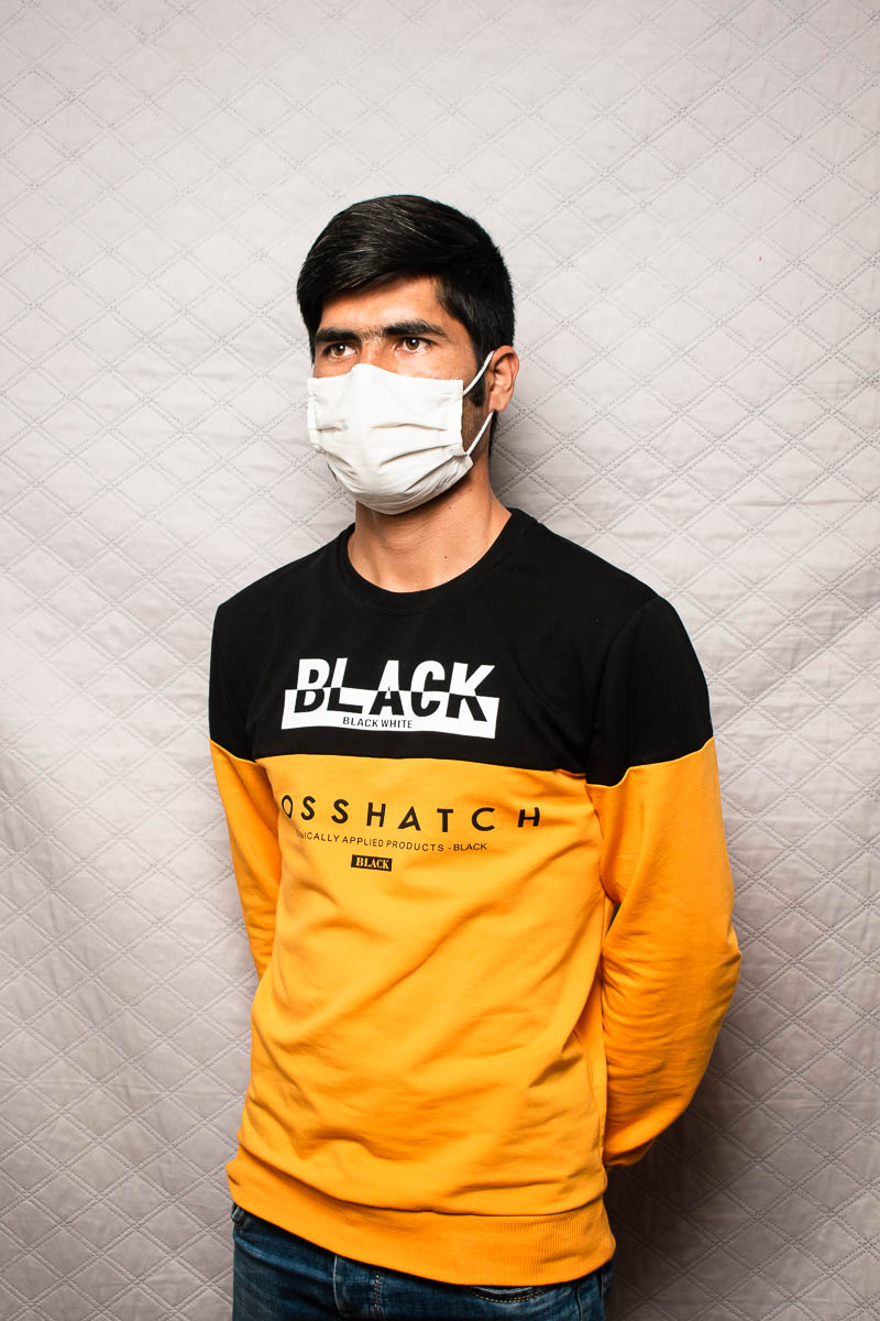 Portrait of Ali wearing a face mask standing with his hands behind his back
