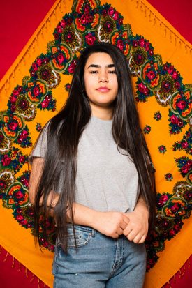 Portrait of refugee Med standing against a background of a yellow traditionally designed shawl