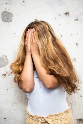 Portrait of refugee Samar hiding their face with her hands