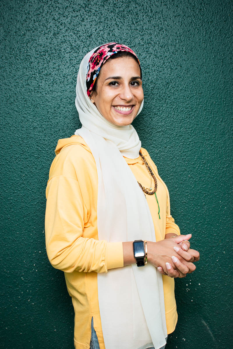 Portrait of refugee Sherouk wearing a hijab and smiling with her hands clasped