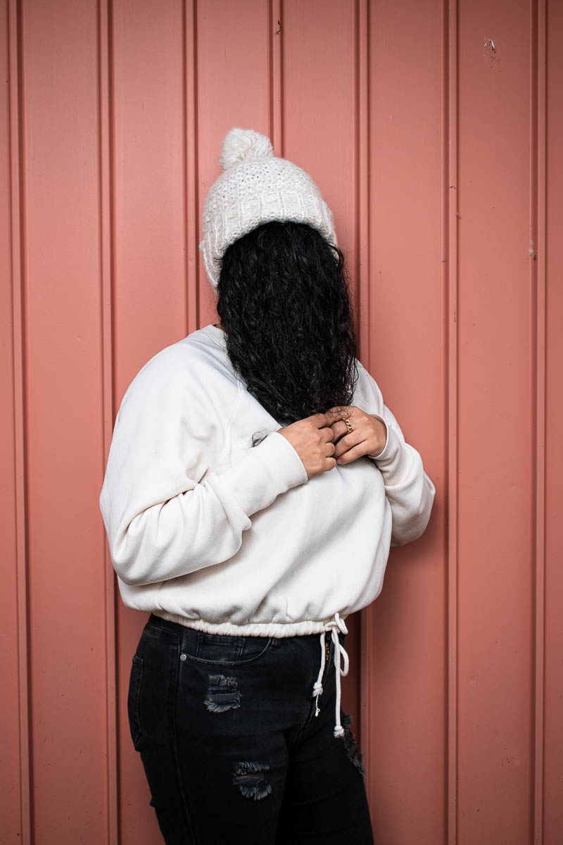Portrait of refugee Shima wearing a woollen cap using her hair to hide her face