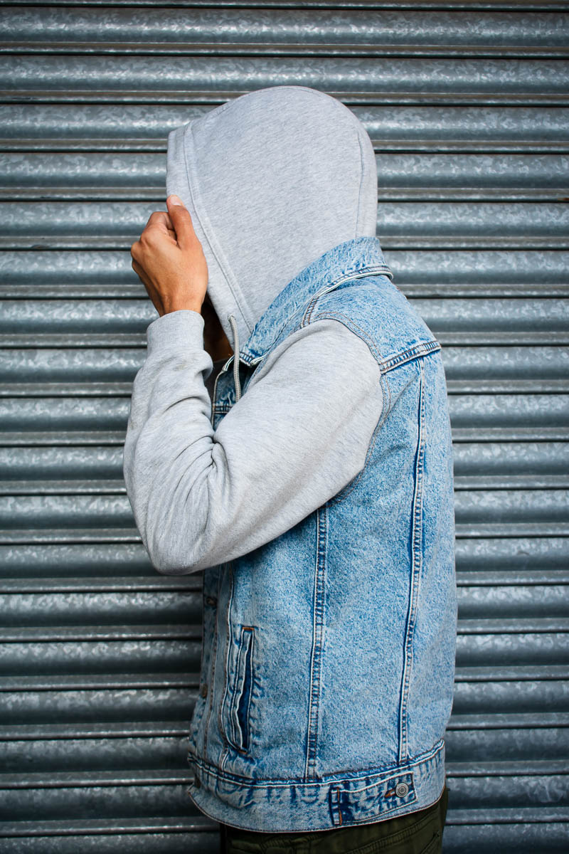 Portrait of refugee Mustapha's side profile , their face hidden with their hand holding the hood up