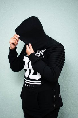 Portrait of refugee Tina Moradi using their hands to pull their hoodie to hide their face