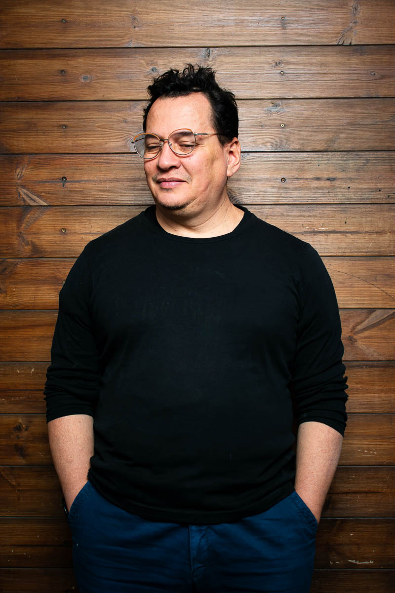 Portrait of refugee Macgregor standing with his hands in the pockets of his jeans looking down smiling