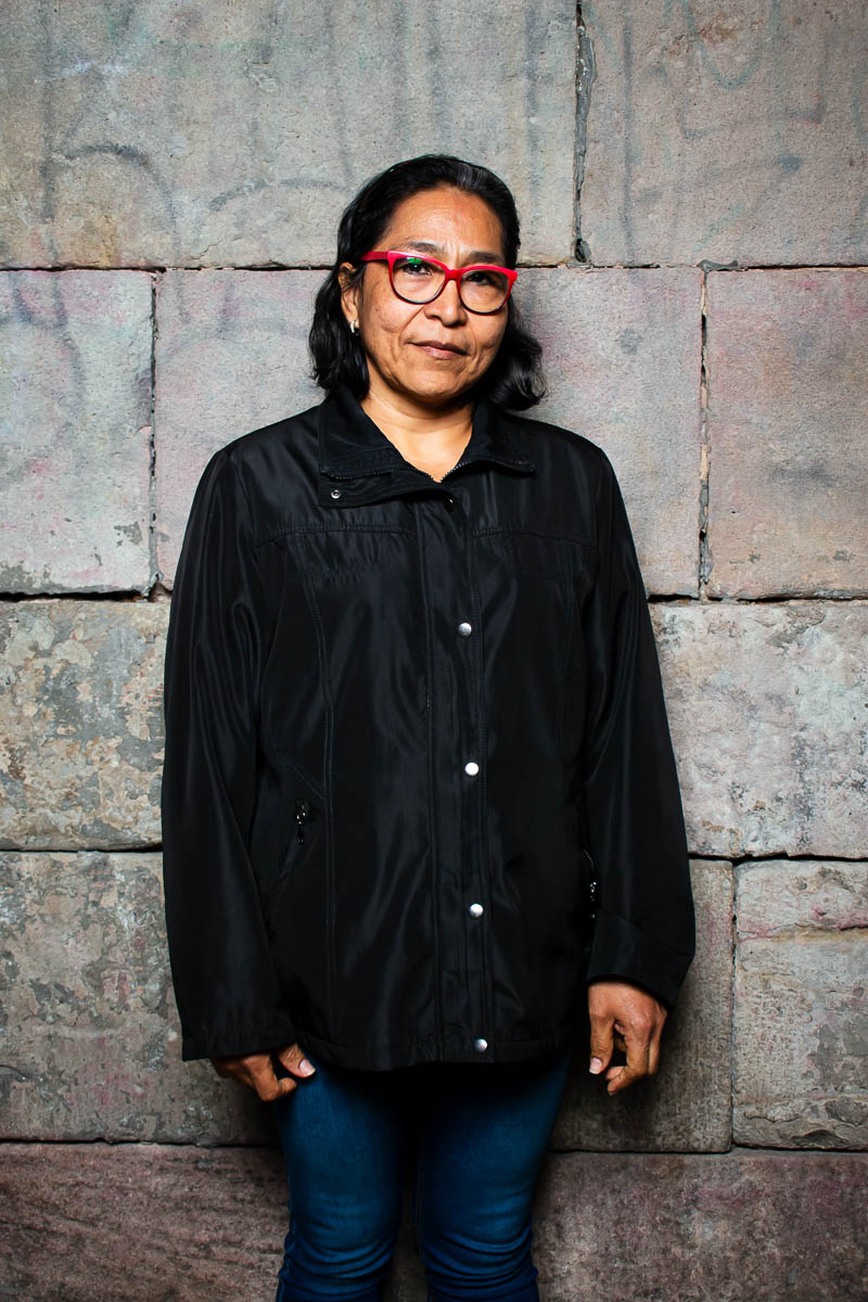 Portrait of refugee Rosa standing against a brick wall