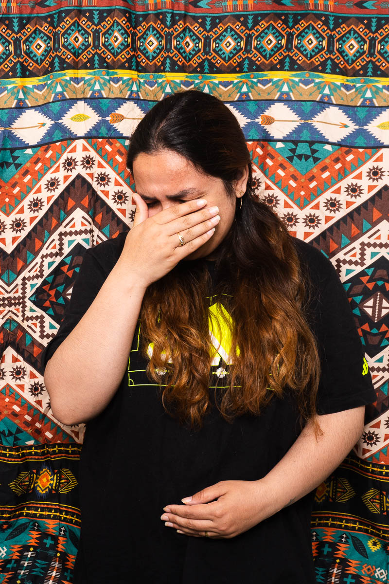 Portrait of Bahshta, covering her face with her hand, has long curly hair wearing a black shirt