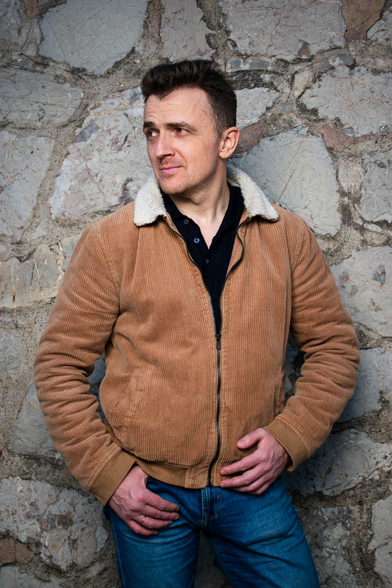 Portrait of Serhii Antonick, not facing directly in the camera wearing a brown leather jacket and denim pants