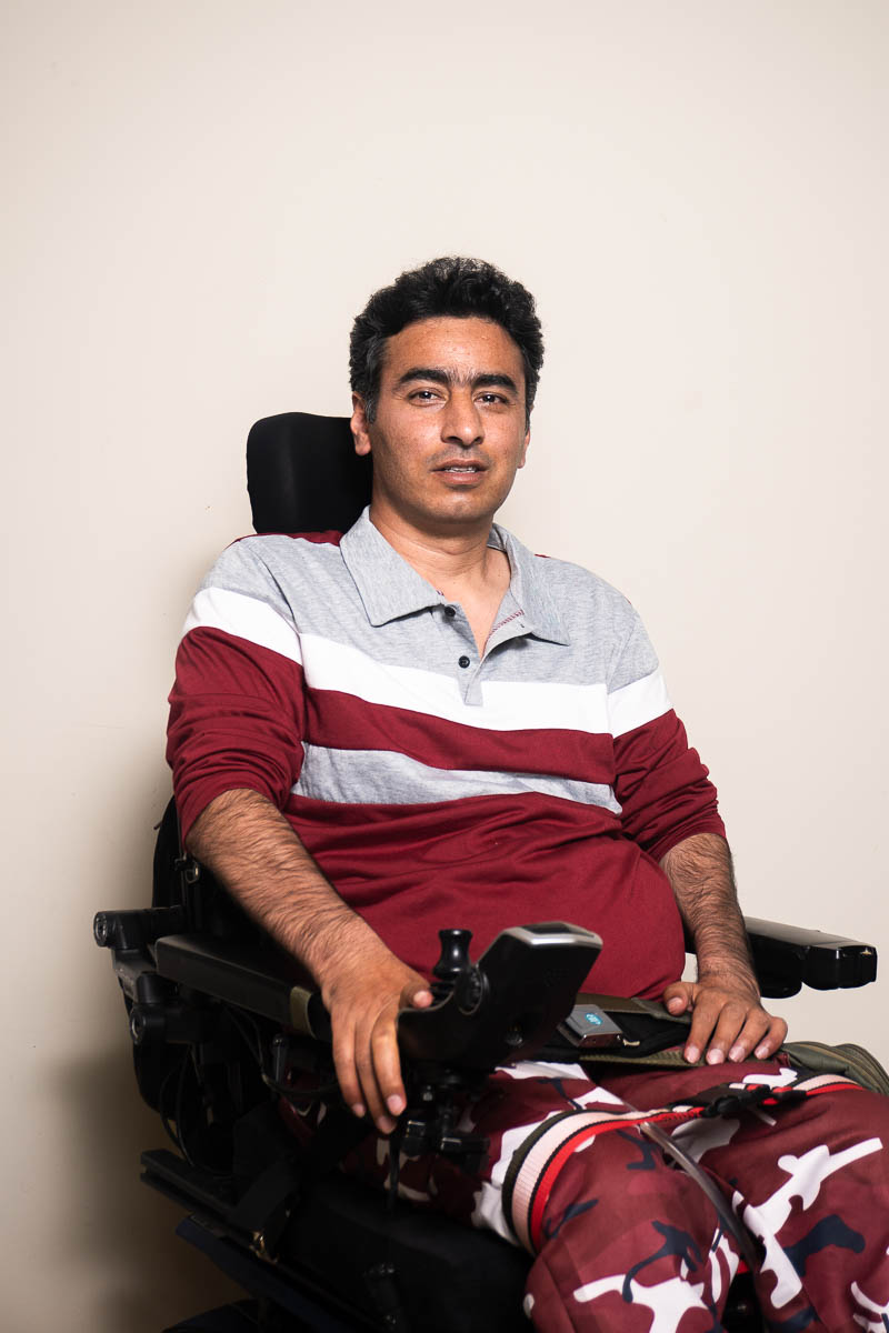 Portrait of Nazir, sitting down while looking at the camera, wearing a red shirt with touch of gray in it.