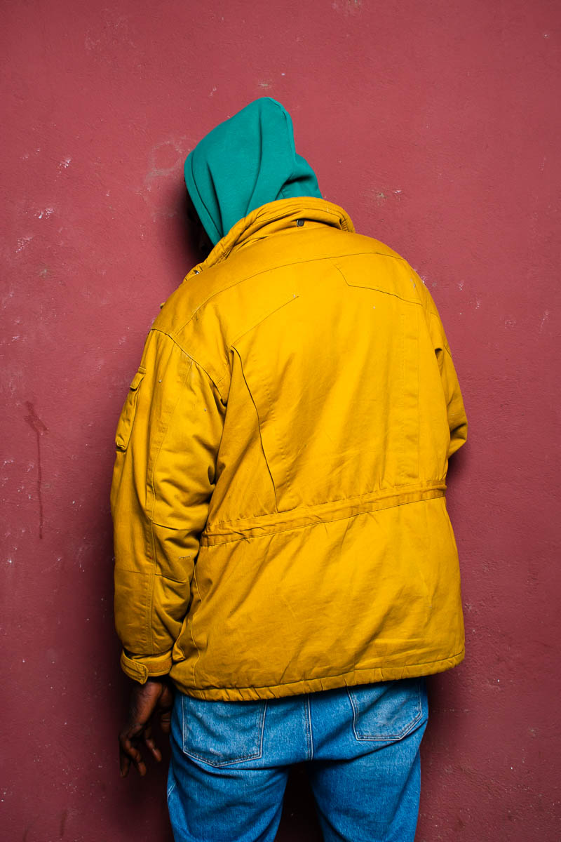 Portrait of Emmy, hiding from the camera wearing a cloth that covers her head and a yellow jacket