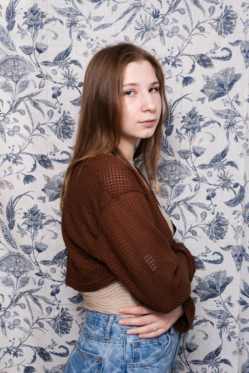 Portrait of Elizaveta, in a side-view pose looking neutral at the camera and is wearing a maroon sweater