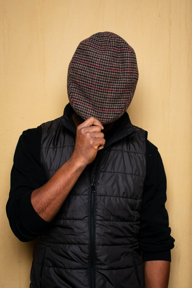 Portrait of Brahim, covering his face with a cloth wearing black jacket.
