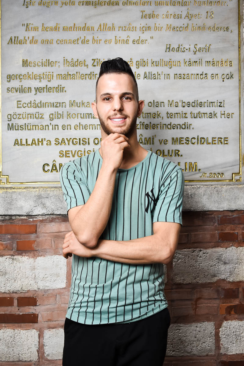 Portrait of Mustafa,smiling at the camera wearing a striped shirt.