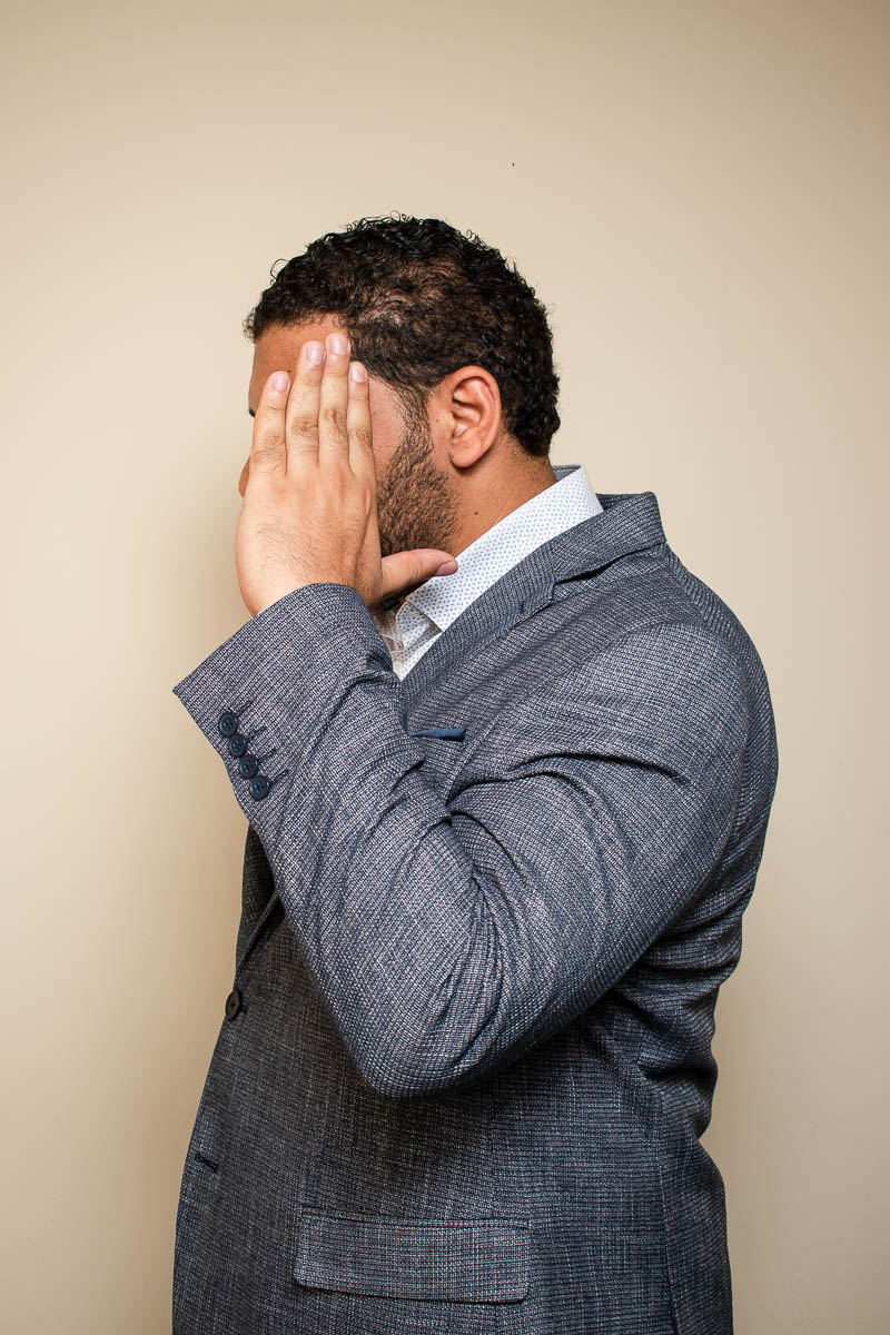 Portrait of Aziz, does not want to show his face to the camera and is wearing a gray suit.