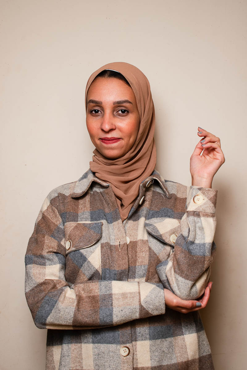 Portrait of Shorouk, facing the camera smiling a bit wearing a stripe jacket and a cloth that covers her head